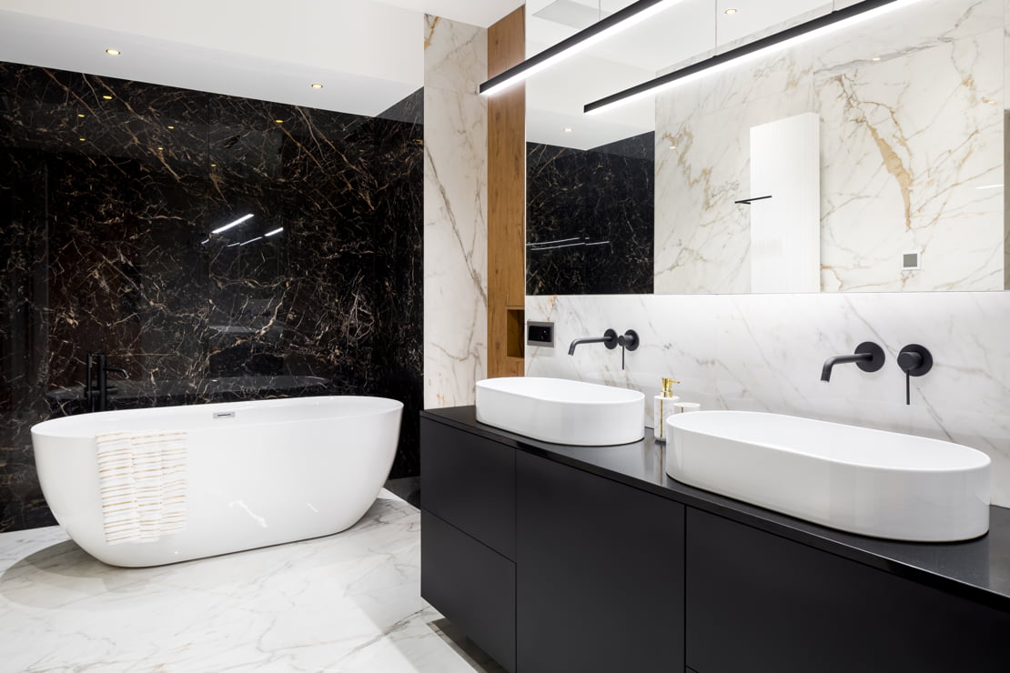 Luxury bathroom with double washbasin, built-in black taps and a bathtub at the back of the room