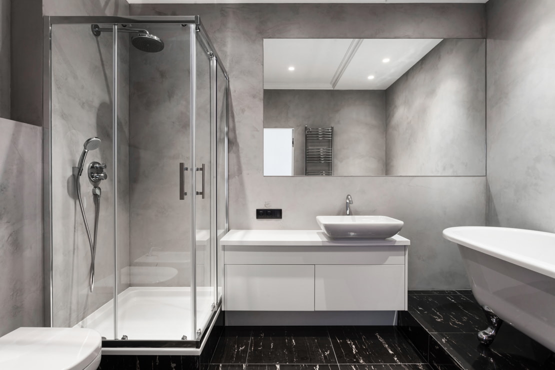 Microcement on the walls of a double-height bathroom with a bathtub.