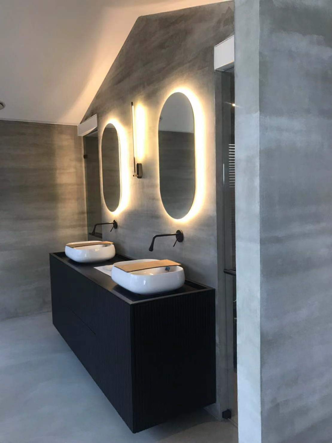 Microcement on the floor and walls of a miminalist bathroom decorated with black taps.